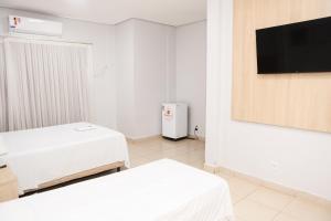 a white room with two beds and a tv at Mais Hotel in Araguaína