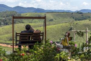 two people sitting on a bench looking out over the hills at Pousada Lago dos Sonhos in Piracaia