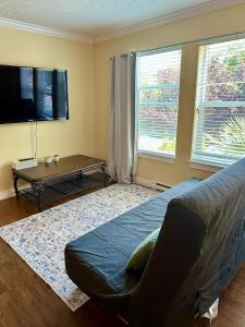 a bedroom with a bed and a table and two windows at Sunny 1BR by Galloping Goose in Victoria