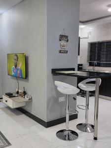 a kitchen with two bar stools and a tv on a wall at DailyPunch Apartment in Kitwe