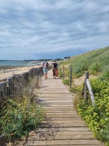 two people walking down a wooden path on the beach at Appartement 30 m de la mer in La Turballe