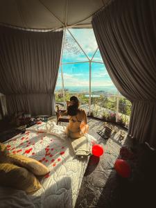 a woman sitting on a bed in front of a window at Domos Mirador Romantic Private Honeymoon Glamping in Miramar