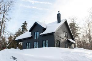 a black house with snow on the roof at Cozy Cottage, The Getaway in Quebec in Brownsburg