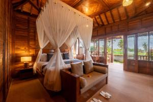 a bedroom with a canopy bed with a couch and windows at Uma Sunset Villa in Ubud