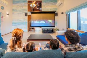 a family sitting in a living room watching tv at まるで映画館 本格シアター 寝室6部屋 大家族大集合 海まで徒歩すぐ ---オーシャニア一宮--- in Ichinomiya