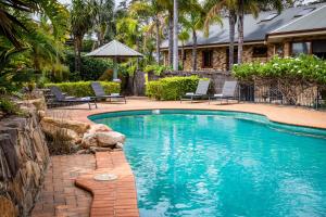 a swimming pool with chairs and a house at Robyn's Nest Lakeside Resort in Merimbula
