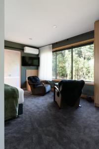 a bedroom with a bed and two chairs and windows at Moss Wood Lane: Peaceful Bath Hideaway in Spreyton