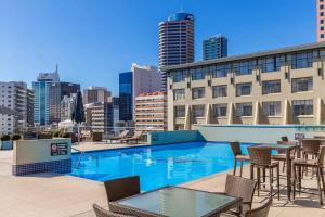 a pool on the roof of a building with chairs and tables at Sky Tower Studio - Pools, Spa, Gym & Super King in Auckland