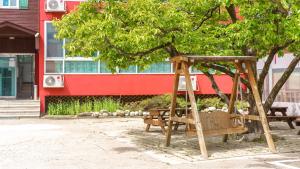 a wooden swing under a tree in front of a building at Goseong Gamnamu Pension in Goseong +1 photo