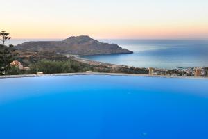 a blue swimming pool with a view of the ocean at Stefanos Village Hotel in Plakias