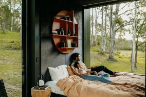 a couple sitting on a bed in a room with a window at The Lantern - a Huch experience in Wollombi