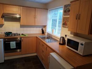 cocina con armarios de madera, fregadero y microondas en Sea Glass Cottage en Sunderland