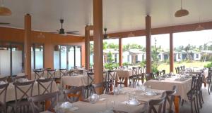 a dining room with white tables and chairs and windows at ANORA Homestay in Vũng Liêm