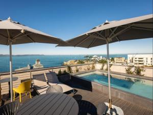 a balcony with a swimming pool and tables and umbrellas at Hermanus Waterfront Boho Studio Apartment, Whale Coast Hideaway in Hermanus
