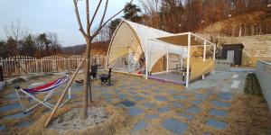 a tent with a tree and a chair in a yard at The Hill Glamping in Yeoju