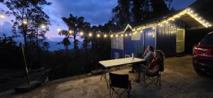 two people sitting at a table in front of a house at Kithul Cottage in Nuwara Eliya