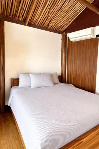 a bedroom with a bed with white sheets and a ceiling at Thani's Little Cabin Rental - Native Room in Caibiran