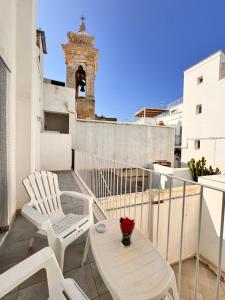 a balcony with two chairs and a table and a clock tower at Petali Rosa - Dimora Antica Roma in Polignano a Mare