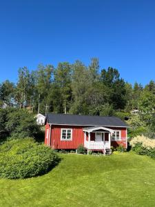 a red house with a black roof on a green field at Sjönära stuga i flogned in Åmotsfors