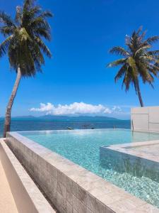 a swimming pool with two palm trees and the ocean at Pano Samui Beachfront Villas in Nathon Bay