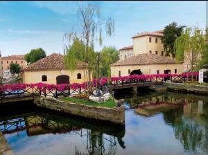 a bridge over a river in a town with pink flowers at "Le Betulle 10" cinque minuti dal mare, Self check in in Bibione