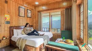 a woman sitting on a bed in a room with a window at Zostel Homes Khajjiar in Chamba