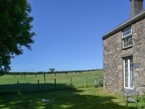 a stone building with chairs and a field in the background at Bodwi Isaf in Abersoch +6 photos