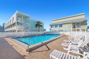 a swimming pool with white chairs and a building at Boardwalk Unit E4 in Pensacola Beach