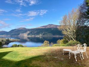 two white chairs sitting on the grass near a lake at Foyers Lodge in Foyers