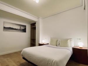 a white bedroom with a bed and two lamps at Apartamento en Eibar in Éibar