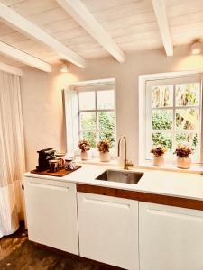 a white kitchen with a sink and two windows at Casas das Piçarras - Alentejo in Piçarra