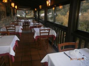 un restaurante con mesas y sillas blancas y ventanas en Hostal El Forn, en Beget