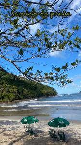 two green beach chairs and umbrellas on a beach at Casa Aroeira Sahy in Barra do Sahy