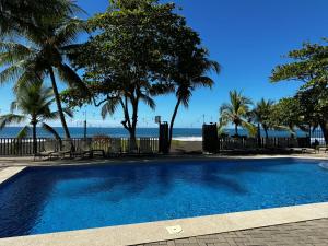 a swimming pool with palm trees and the beach at BigWave Costa Rica in Playa Hermosa