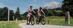 two people riding bikes on a road with a mountain in the background at LoveNest Hungary in Győrújbarát