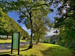 a sign in the grass next to a road with trees at Scandi Style Bracken Lodge with Private Decking Sleeps 6 in Chudleigh Knighton