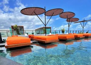 a pool with orange chairs and umbrellas in the water at Edition 201- Flat aconchegante no Cabo Branco - ASKA in João Pessoa