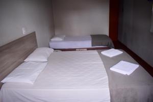 two beds in a small room with white sheets at Hotel Imperador Caldas Novas - GO - Facil acesso aos parques aquaticos e polo gastronômico noturno in Caldas Novas