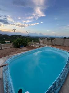 a blue swimming pool with windmills in the background at Chalé Vista Encanto dos Montes in Monte das Gameleiras