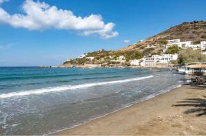 a beach with houses on a hill next to the ocean at Sunset Realty in Ano Syros