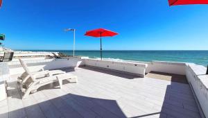 a patio with a red umbrella and chairs and the ocean at Charming & Cozy Beachfront Condo Las Olas I 19 in Puerto Peñasco