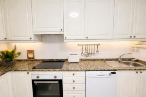 a white kitchen with white cabinets and a sink at Holibai Amieiro Apto amplio y luminoso cerca de la playa, Baiona in Baiona