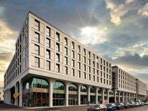 a large white building with cars parked in front of it at ibis Styles Muenchen Perlach in Munich