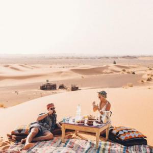 two people sitting at a table in the desert at Fantastic Luxury Dunes Camp in Merzouga