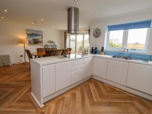 a kitchen with white cabinets and a large window at Farne Cottage in Beadnell