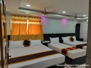 a room with two beds and an orange curtain at Hotel Grand Arputha in Velankanni