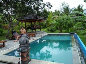 a man sitting on a bench next to a swimming pool at Pondok Balian in Selemadeg