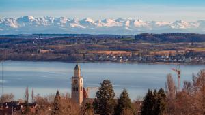 a church on the shore of a lake with snow covered mountains at Hotel Capri in Überlingen