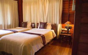 a bedroom with two beds and a table with a lamp at Chuanthanapanya Resort in Amphoe Sawang Daen Din
