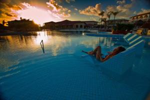 a woman sitting in a swimming pool at sunset at Grand Palladium Imbassaí Resort & Spa - All Inclusive in Imbassai